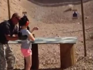 Menina e instrutor apontar metralhadora para um alvo.