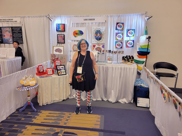 This is a photo of Laura Bundesen with her artwork at the Society of Neuroscience 2023.