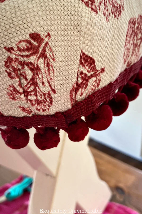 Corner of upholstered bench with red pom pom trim