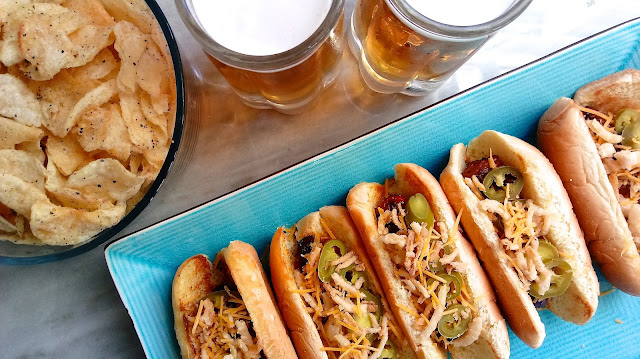 Game Day Jalapeño Cheddar Bacon Dogs on a serving tray next to a bowl of chips and two glasses of beer