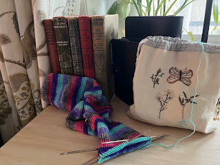 handknit sock with embroidered knitting bag in front of vintage mystery novels