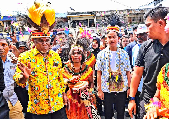 Dari Cenderawasih Jadi Cenderamata Yanto Eluay (batik baju kuning) bersama Cawapres Gibran Rakabuming Raka (baju kotak biru putih) yang menolak memakai mahkota burung cenderawasih saat kampanye di Jayapura pada Jumat 26 Januari 2024 - (TKN)