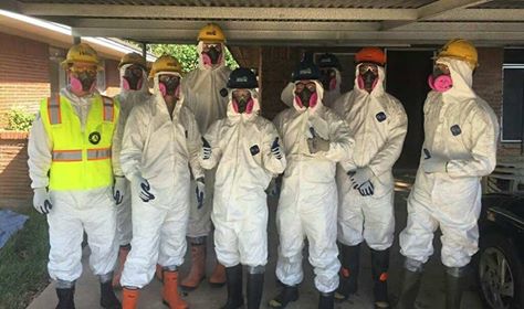 A group of AmeriCorps members are wearing white Tyvek suits and yellow hard hats to protect themselves before they enter a home for debris removal.