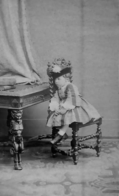 Carte Visite fotografía niña sentada.  Mesa y silla talladas Dragon & Cie París hacia 1880 XIX En este caso la niña esta sujeta con una cinta en la cabeza con la silla.