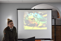 Nasz gość pani Karolina Piasecka prezentuje dzieciom zdjęca płazów wyświetlone na ekranie za pomocą rzutnika.