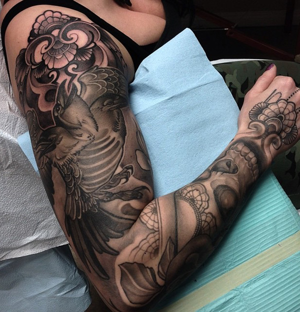 Em tons de cinza de manga tatuagem sobre corvos. Você pode imediata e o corvo voando alto e forte sobre a parte superior dos braços. Você também pode ver um pouco de floral design, bem como alguns temas tribais também. 