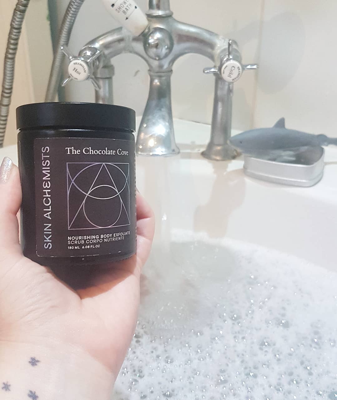 Skin Alchemists Chocolate Cove body scrub held up in a relaxing bath