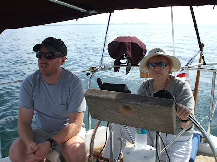 Damon's mom is at the wheel of a sailboat, wearing a jaunty sun hat.  Damon is sitting beside her, probably thinking "life is good."