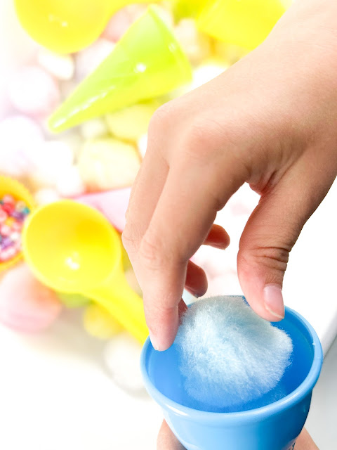 a child's hand putting pom poms in a cone.