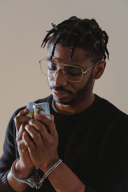 Black Man In Handcuffs Holding Rolls of Money