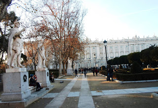 La estatuas forman hilera, flanqueando bancos de piedra, al fondo el Palacio Real y en medio los jardines.