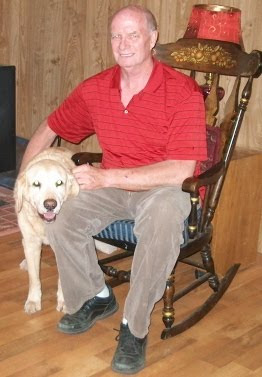 Larry in rocking chair with his arm around yellow Lab Galleon