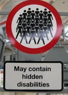 A round street sign with a red edge, inside it has multiple stick people all the same. Underneath the sign is a notice saying May contain hidden disabilities