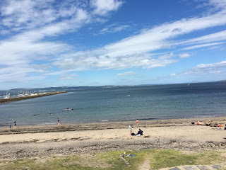 The beach with a few people standing or swimming.