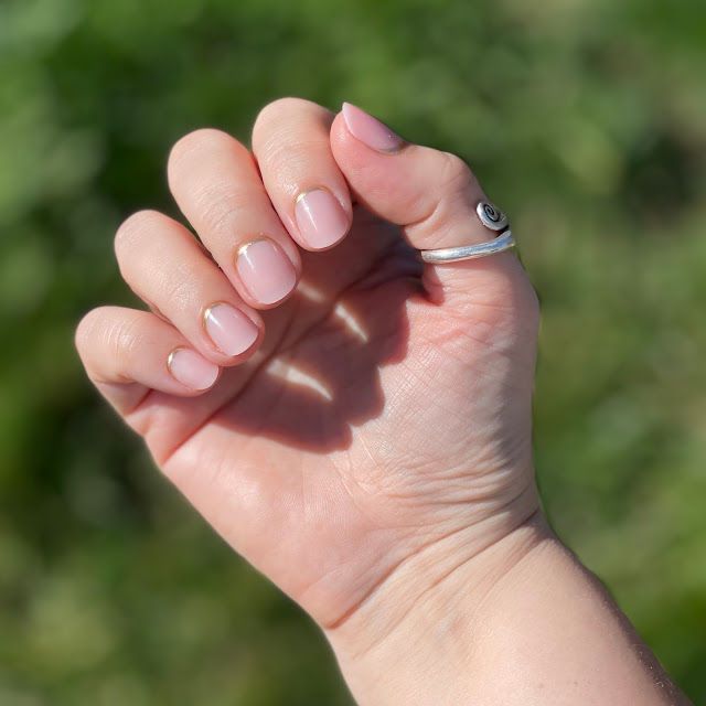 Glamnetic nails after application that have been filed and trimmed on woman's hand over grass in the sun