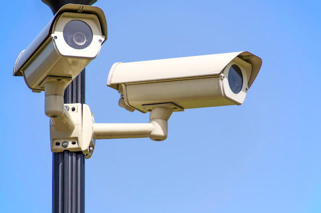 Two security cameras on tall pole with blue sky as background