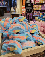 A zoomed in shot of a bunch of car shaped bath bombs with red and blue on them in a large square light brown box on a bright background with love bug bath bomb in white font on a black card next to it