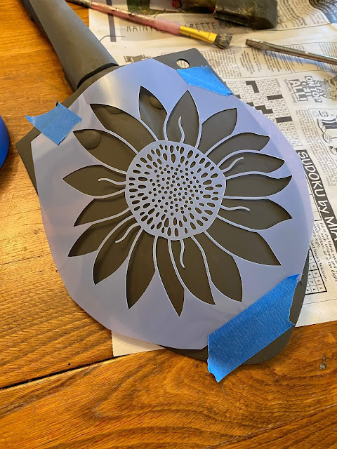 Photo of a Hobby Lobby sunflower stencil taped to a shovel head.