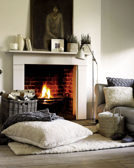 Warm textiles and burning fire in this cozy fireplace setting by The White Company.