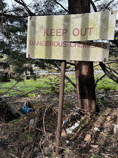 A photo of a rectangular sign on a rusty metal pole.  The sign has a split along one side.  The sign reads - Keep Out Dangerous Chemicals.  Photo by Kevin Nosferatu for the Skulferatu Project.