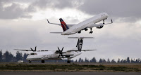 A Delta jet takes off in view of an Alaska Airlines plane that just landed Wednesday, Dec. 16, 2015, at Seattle-Tacoma International Airport. A proposed emissions standard for international aviation was approved Monday. (Credit: AP Photo/Elaine Thompson) Click to Enlarge.