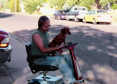 Dachshund Pup named Dixie riding with Jimmy down sidewalk on an Amigo scooter