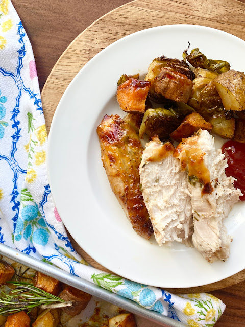 Sliced turkey & veggies on a white plate next to a flowered towel and sheet pan.