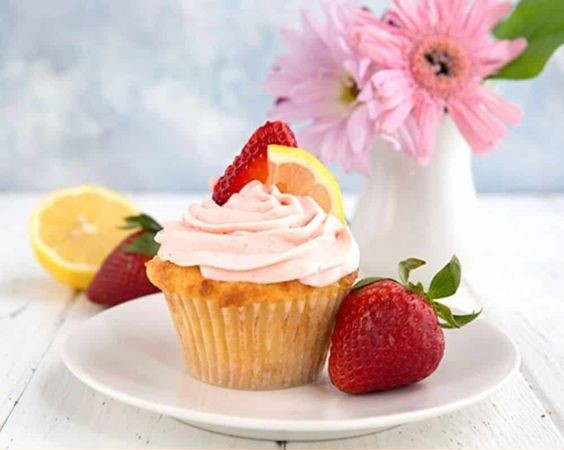 A strawberry lemonade cup cake on a countertop with a vase full of flowers in the background.
