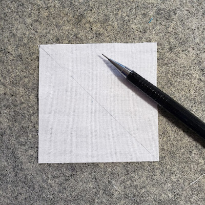 A mechanical pencil with a square of fabric which has a diagonal line drawn on it from corner to corner.