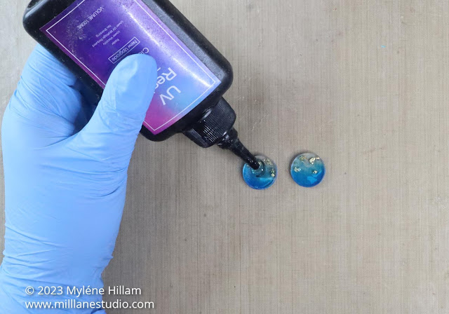 Gloved hand holding a bottle of UV resin and squeezing UV resin onto the resin circles