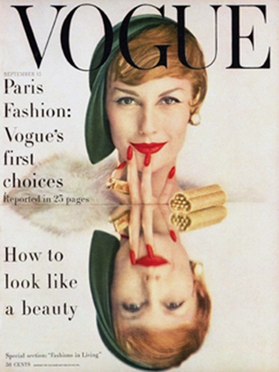 Model Mary Jane Russell's face with reflection on mirrored table top, in green hat with red lipstick and nails
