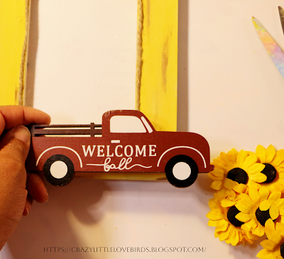 Hand holding red truck decoration to bottom section of yellow painted frame