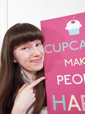 Smiling and pointing to 'Cupcakes Make People Happy' poster
