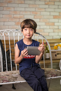 a child wearing earphones holds a tablet