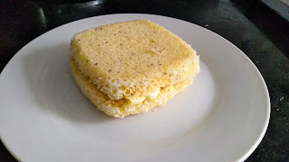 Sanduíche de pão de farinha de arroz com queijo mussarela num prato branco em cima de bencada de pedra preta