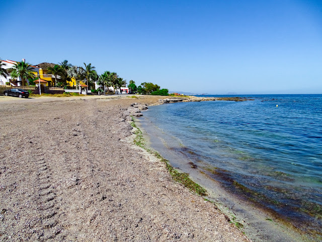 Playa llana de arena fina con urbanizaciones a su espalda y las azules aguas del mar a su frente