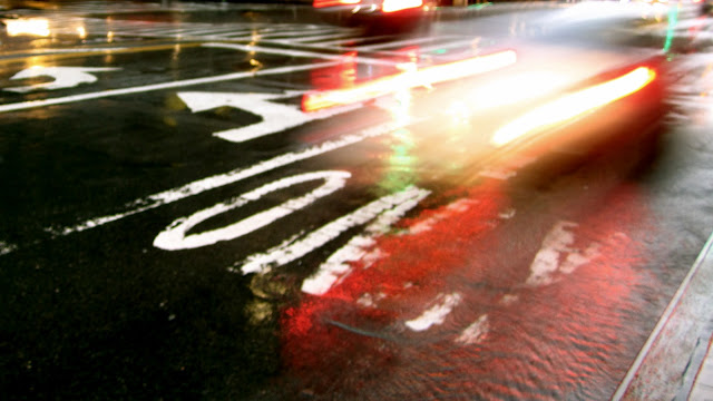 A Yellow cab passes by on a rain-glazed street.