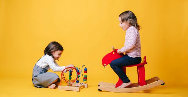 Two girls are playing: one with a toy moving small balls in a spiral, the other on a riding rocking toy.