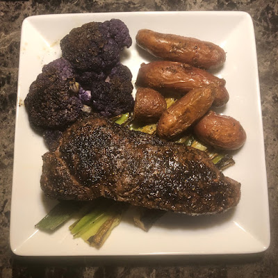 Zhatar seasoned New York Strip grilled rare on a bed of grilled leeks with grilled purple cauliflower and oven roasted rose fingerling potatoes