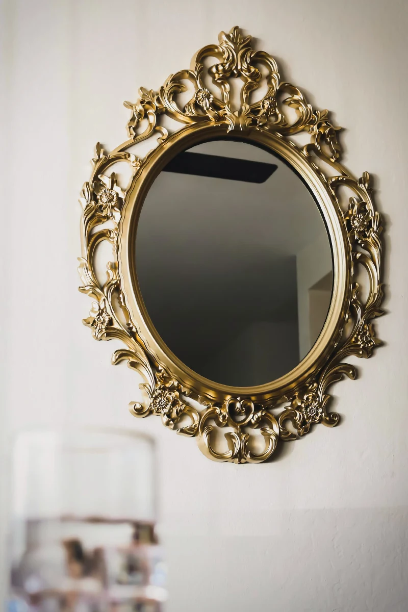 beautiful mirror in a posh bronze frame is hanging on a white wall