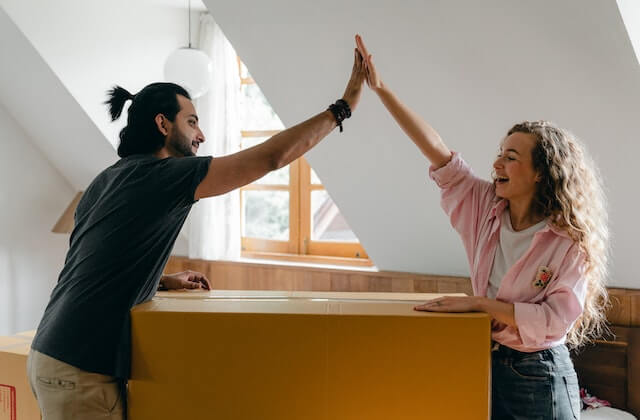 Man and woman doing high-five with boxes in new home