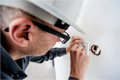 An electrician with a helmet working on a plug in a wall.