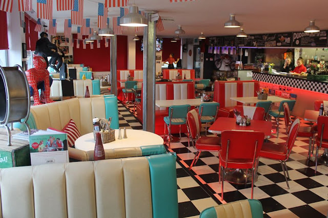 Interior of A21 Diner in East Sussex, featuring red, white and blue leather booths, and American flags hanging from the ceiling