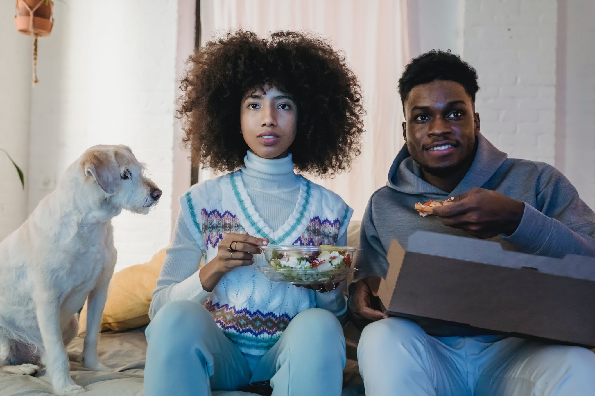 Two adults eating popcorn and watching TV with dog. Photo by Andres Ayrton from Pexels