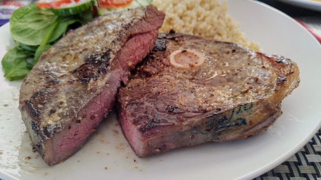 A cross-section of a medium rare reverse-seared lamb leg steak on a white plate with spinach salad in the back.