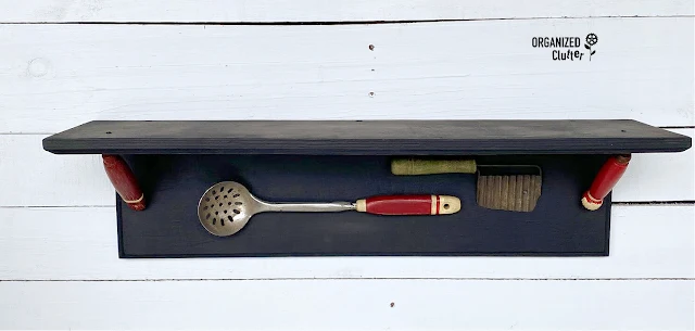 Photo of a farmhouse kitchen shelf with attached faux utensils.