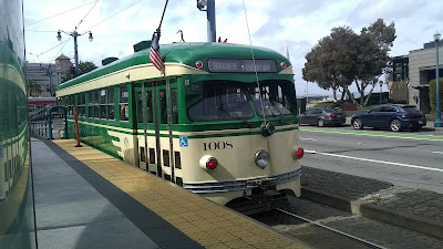 Old-fashioned streetcar, cream and green body, seen from a platform.