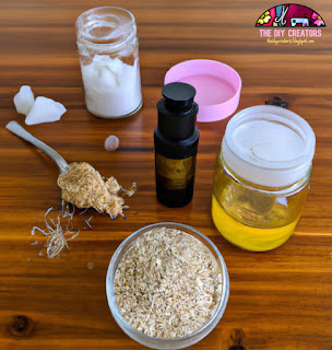 Image: A picture of various DIY beauty product ingredients displayed on a wooden table. The ingredients include honey, coconut oil, oatmeal, sugar, and essential oils.