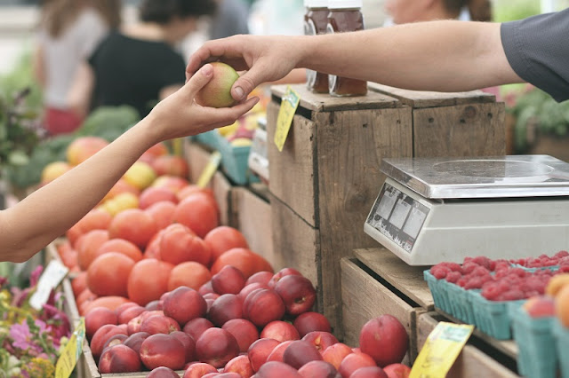 A woman's hand holding a peach at a farmers market.