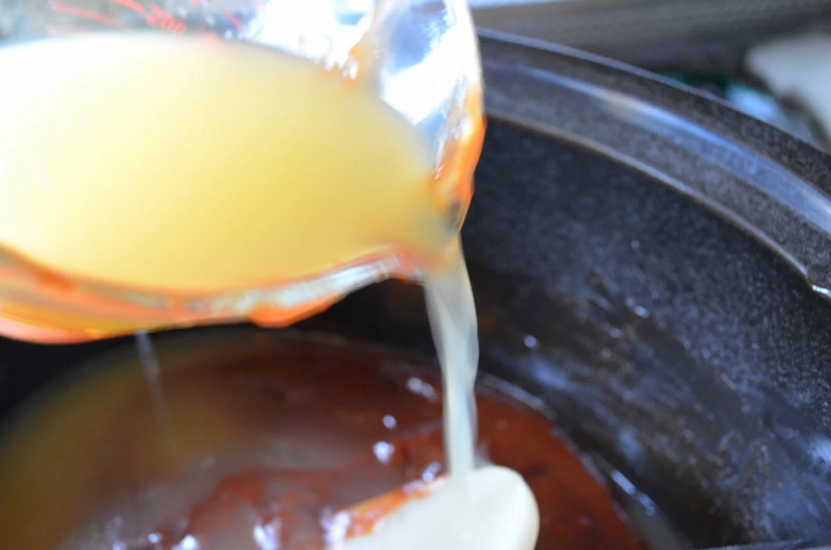 Crock Pot Pulled Chicken Homemade BBQ Sauce being mixed together in a black crock pot with chicken broth being poured in.